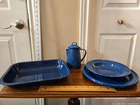 Side view of the full set showing teapot, casserole dish, bowl, and three plates on a wooden surface with a ruler behind for scale.