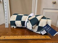 Rolled Old Navy fleece blanket showing green and white checkered pattern with measuring scale beside it indicating size.