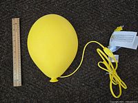 Yellow balloon-shaped wall lamp next to a 12-inch ruler for size reference, showing front angled view and electrical cord.