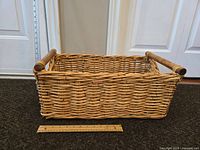Large rectangular woven wicker basket showing side view with wooden handles and a ruler for scale.