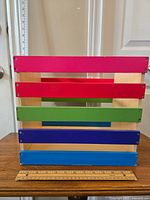 Front view of multi-colour wooden crate featuring pink, red, green, purple, and blue slats and natural wood frame with handle cutouts