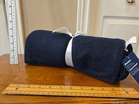 Rolled navy fleece blanket tied with white ribbon placed on a wooden surface with rulers for scale.