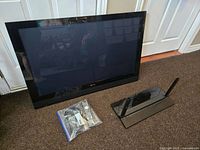 Pioneer Elite 42-inch plasma TV with remote and stand placed on the floor against a door. TV screen is off, black bezel, and a clear plastic bag containing remote and cords in front.
