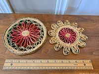 Photo showing two vintage wicker trivets on a wooden surface with a ruler for scale, highlighting size and woven floral details.