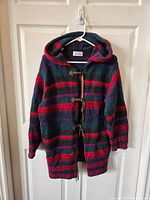 Overall front view of hooded wool sweater jacket featuring bold colorful stripes in purple, red, green, and gray, highlighting the leather toggles.