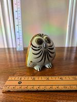 Front view of small hand painted owl figurine on wooden surface with measuring rulers showing about 3 inch height.