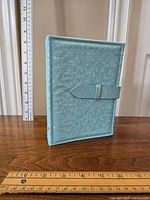 Front and side view of light blue travel earring keeper binder with snap closure, placed next to rulers for scale.