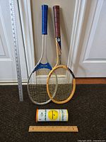 Two vintage tennis rackets side by side, one wooden Spalding and one aluminum Slazenger, with ruler for size reference, and a can of two new Dunlop tennis balls below.