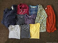 Full view of 10 clothing items laid flat showing variety of colors and styles including sweaters, tops, and shirts.