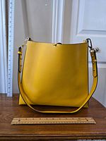Front view of the yellow Zara bucket bag with a ruler placed horizontally and vertically for size reference.