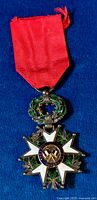Front view of the 19th century French Legion d'Honneur breast badge medal showing the white enamel Maltese cross, green laurel and oak wreath, central blue ring with gold text, and attached red ribbon.