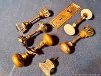 Five pairs of antique doorknobs and a brass door plate arranged on a dark surface
