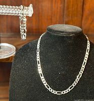 Necklace displayed on black bust with bracelet draped on side support.