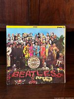 Front cover of The Beatles Sgt. Pepper's Lonely Hearts Club Band album showing detailed, colorful group image and floral "Beatles" text.