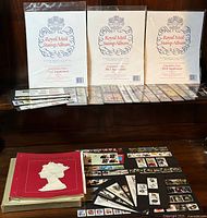 Three sealed Royal Mail Stamp Album supplement packs upright, loose stamps, red binder and additional cream pages below