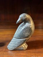 Front left three-quarter view of dark grey soapstone bird sculpture on wooden tabletop