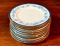 Stack of 10 Noritake Bellefonte bread and butter plates showing side view of thickness and gold-trimmed edges.