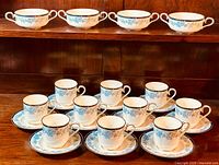 Front view of 4 two-handle bouillon soup cups on top shelf with 10 teacups and matching saucers arranged below on wood shelf.