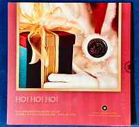 Box front showing festive holiday gift theme with ribbon and a visible coin embedded with Santa Claus design.