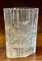 Clear textured art glass vase with icicle-like pattern, standing on wooden surface.