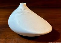 White ceramic bud vase placed on a wooden surface showcasing the asymmetrical body and textured dot pattern near the opening.