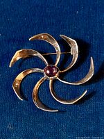 Top view of the brooch lying on a textured dark blue fabric background, showing the full design with the amethyst cabochon in the center.