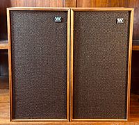 Front view of both speakers side by side showing teak veneer frames and brown grille cloth with metal Wharfedale logos.