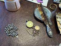 Sterling hand mirror and comb with ornate sterling handles. Comb has breakage; mirror glass scratched. Also shown are two pocket watches, one with a long chain, and silver rosary and hair pin.