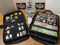 Overhead view of two open black pin binders showing Disney, Hard Rock Cafe, SF Giants and other enamel pins, plus plastic tubs and binders behind