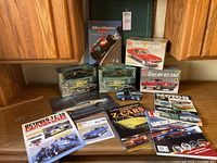 Photo showing boxed model car kits including two AMT Shelby GT kits, two Greenlight Ford Mustang Bullitt kits, and several automotive magazines arranged on a table.