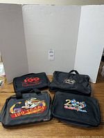 Four black soft zippered pin binder cases on wooden table, front view