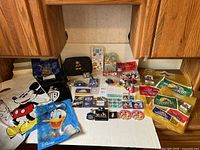 Wide angle shot showing all Disney items including gift bags, pins, and tags arranged on white surface under wooden cabinetry.