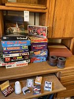 Photo showing stack of boxed vintage classic board games and Backgammon set on shelf with decks of cards displayed below.