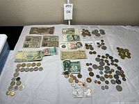 Wide overview of all currency notes and coins laid out on fabric showing multiple denominations of bank notes and a large assortment of coins.