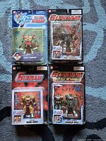 Four sealed Bandai Gundam action figures in original blister packaging laid out on carpet