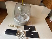 Speaker with transparent glass dome and white/grey fabric bottom part. Includes power supply and user manuals.