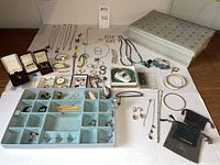Wide view showing assortment of jewelry including necklaces, rings, earrings, bracelets, watches, and jewelry box on white cloth.