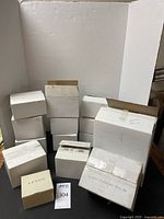 Nine white and branded Lenox boxes arranged on a table, some marked with handwriting, showing the boxed packaging of the ornaments.