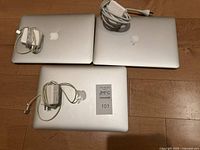 Top view of three closed MacBook laptops laid on floor with three white MagSafe chargers placed on laptops.