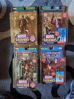 Four Marvel Legends boxed figures: Daredevil, Galactus series Professor-X, Silver Centurion Iron Man, and Falcon on carpet with packaging showing character and accessories