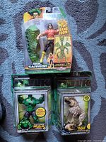 Front view of three unopened Marvel Legends figures: Doc Samson with dragon parts, Hulk with sound feature, Hulk Dog, on blue patterned blanket.