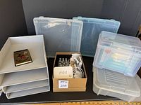 Photo showing multiple clear plastic boxes for storage, a small box with mint stamp maker and wooden stamps, and a flat item that appears to be a Mickey Mouse themed paper pad.