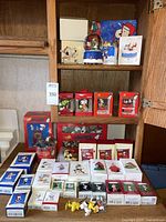 Wide view of multiple shelves with boxed Hallmark Keepsake Peanuts figurines and ornaments, light sets, key chains, and other Christmas decorations all in original packaging.
