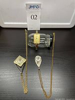 Lot overview of one gold-tone watch bracelet and two watch pendants on gold chains placed on a dark surface with a clear small jar as stand for watch bracelet.