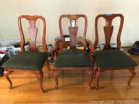 Three dining chairs showing wood frames, carved backs, and green tapestry seats. Chairs comprise arm chairs and side chairs.