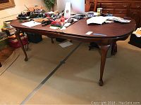 Solid wood dining table with a cluttered tabletop, showing overall condition and leg design.