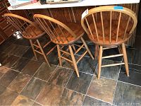Three matching solid wood bar stools placed side by side on a tiled floor, showing the overall look and style.