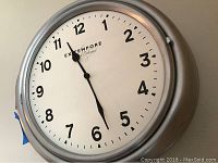 Front angled view of Extempore wall clock with silver metal frame showing clock face and hands indicating time.