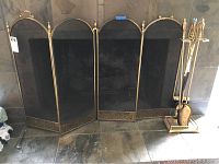 Four-panel brass fireplace screen with mesh and brass trim, displayed against stone wall.