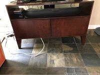TV stand front view with cabinet doors closed, showing dark wood finish and simple mid-century style design.